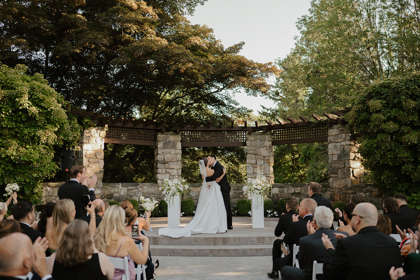 Newlyweds sharing their first kiss at the outdoor stone altar as guests clap in celebration.